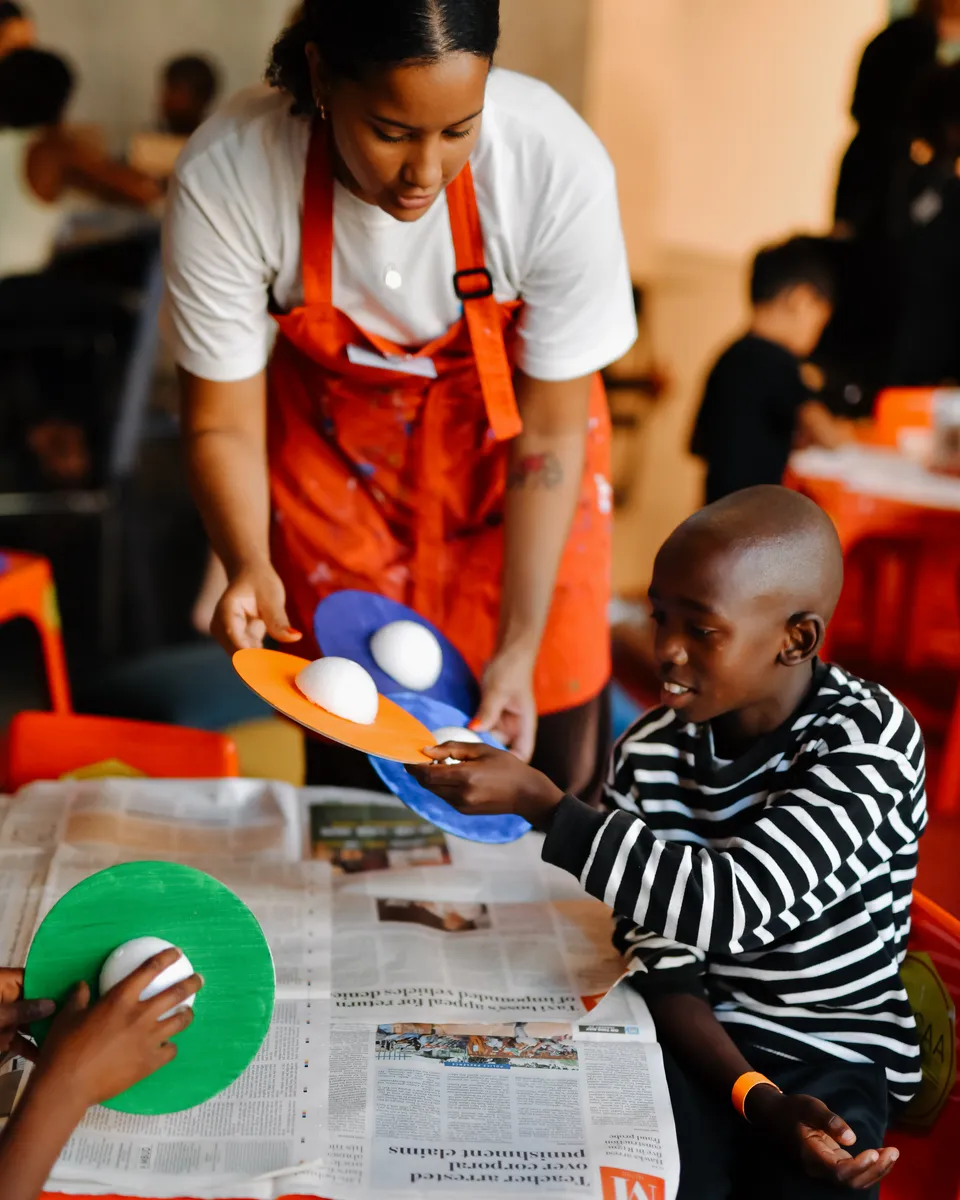 An educator hands out art materials to children during a workshop